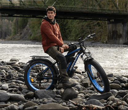 Man sitting on SENADA ARCHON PLUS fat tire electric bike by a rocky riverside, ideal for off-road adventures and long-distance riding.