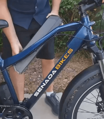 Person showing removal battery for easy charging of SENADA SABER PLUS electric bike with all-terrain capability and advanced safety features.